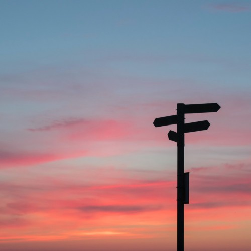 A street sign sits in the foreground of a colourful sunset.